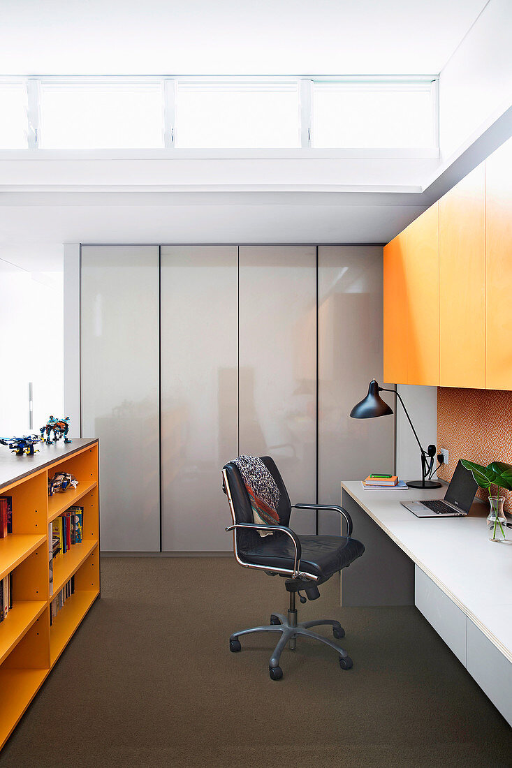 White desk top, black swivel chair and orange wall cabinet in the study
