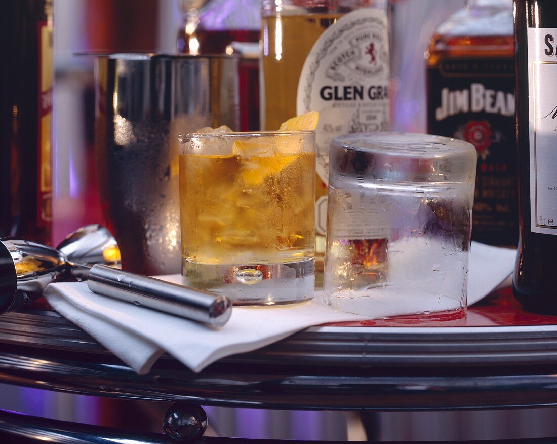 Whiskey Glen Grant mit Eis im Glas & Whiskeyflaschen auf Bar