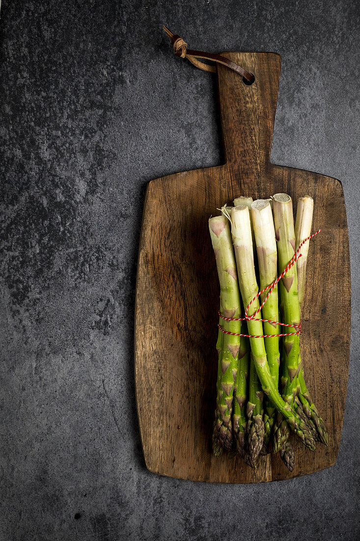 Asparagus with a little red rope on a wooden plank at a black canvas
