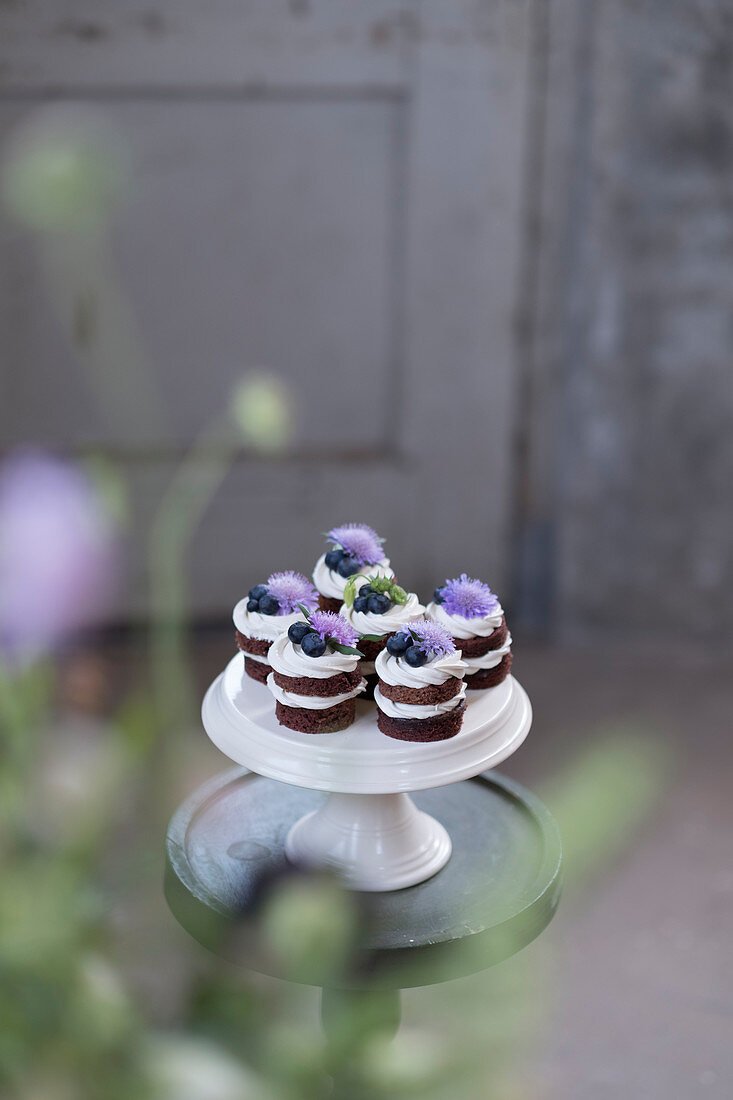 Schokoladen-Cupcakes mit Heidelbeeren und Kornblumen auf Kuchenständer