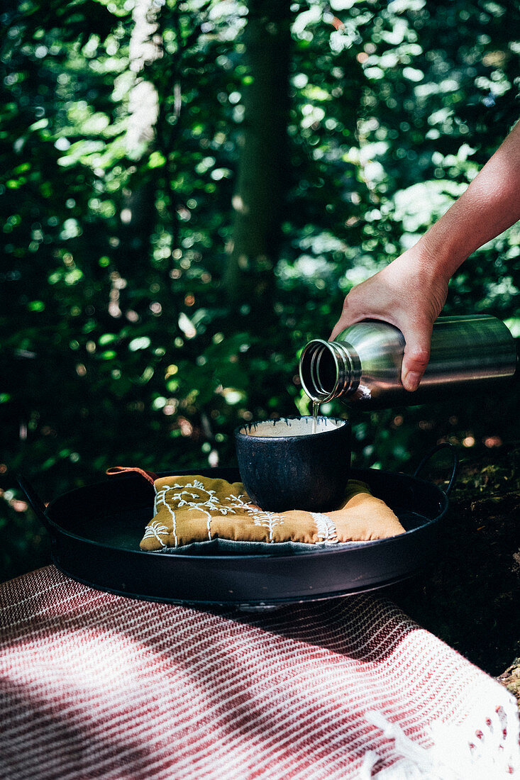 Hand giesst Tee in Tasse beim Picknick im Wald