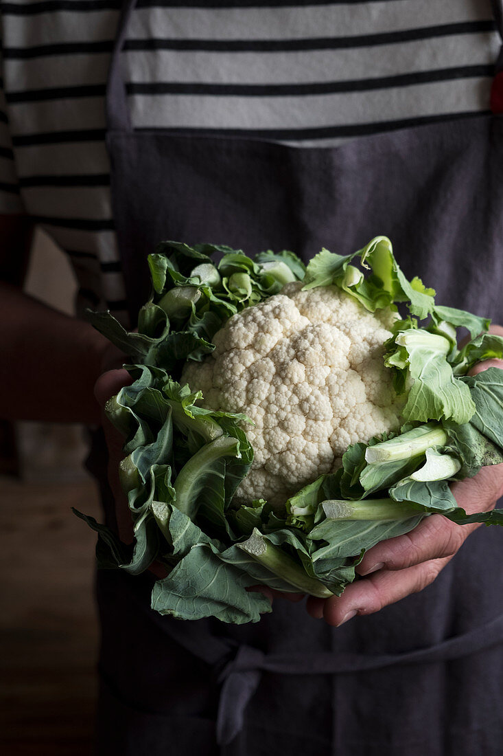 A men with a linen apron holding a cauliflower in his hands