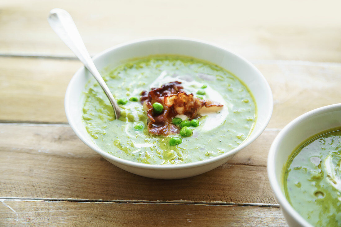 Creamy green pea soup with fried bacon and herbs
