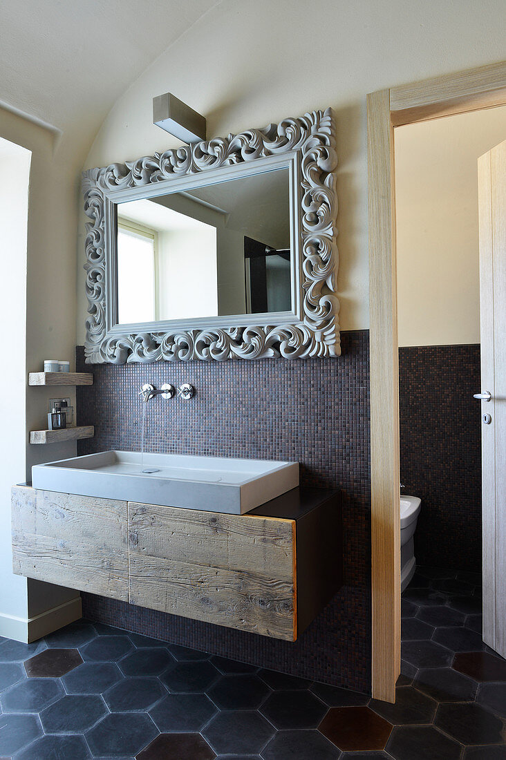 Wandspiegel mit kunsthandwerklichem Rahmen über Betonwaschbecken im Designerbad mit Zementfliesen