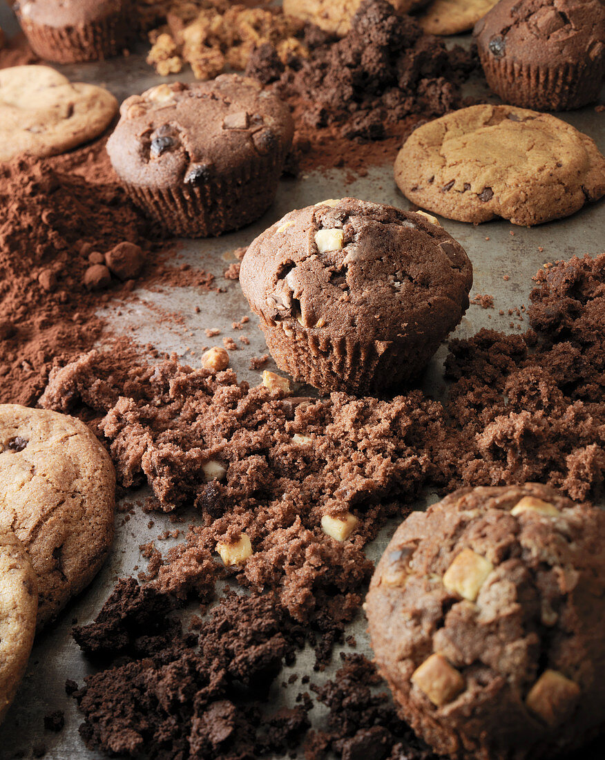 Schokomuffins und Cookies auf Backblech mit Kakaopulver und Krümeln