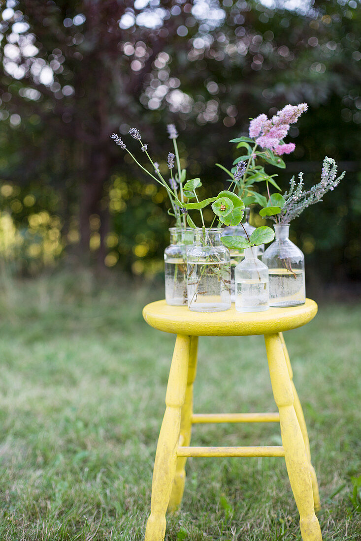 Apothekerflaschen mit Gartenblumen auf einem gelben Hocker