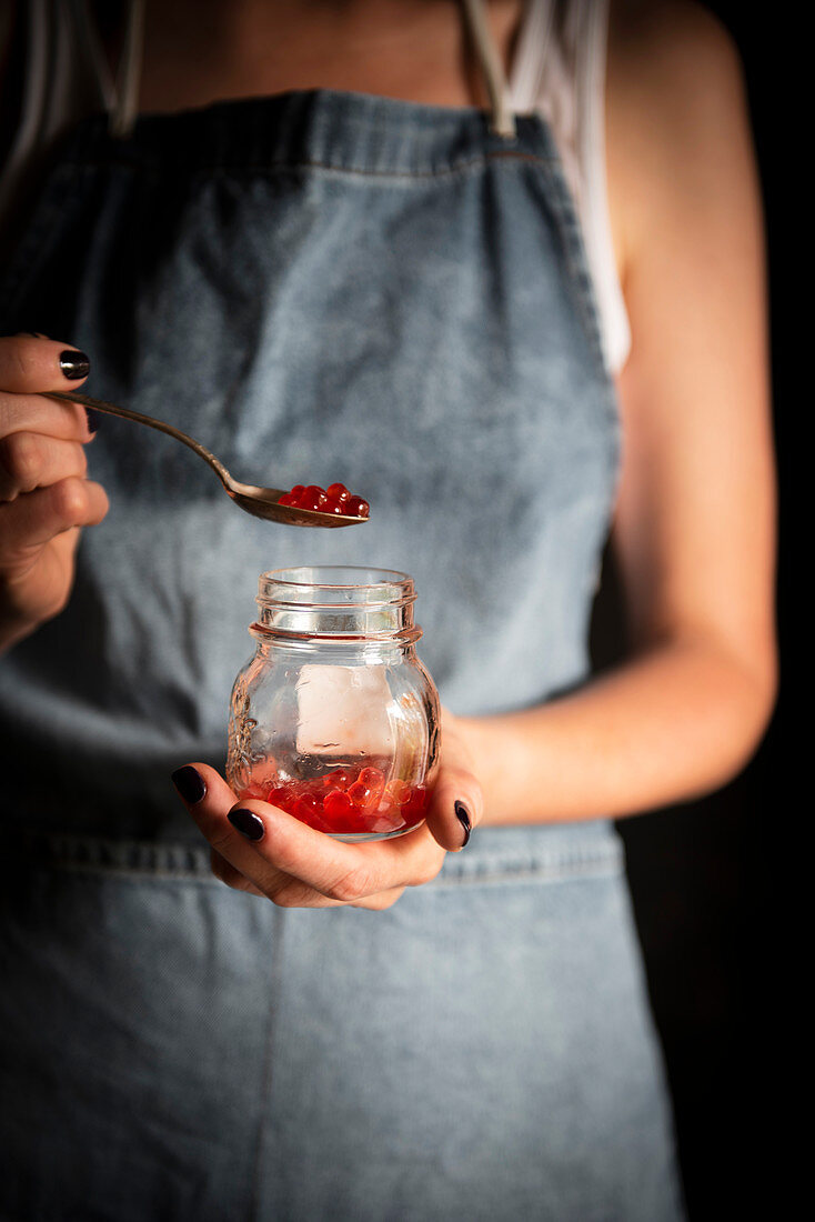 A woman holding a glass and spoon with red caviar