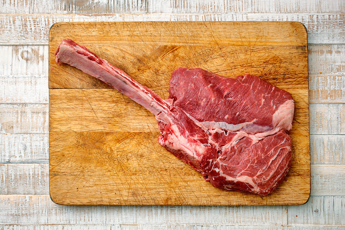 A raw veal tomahawk steak on a wooden chopping board (top view)