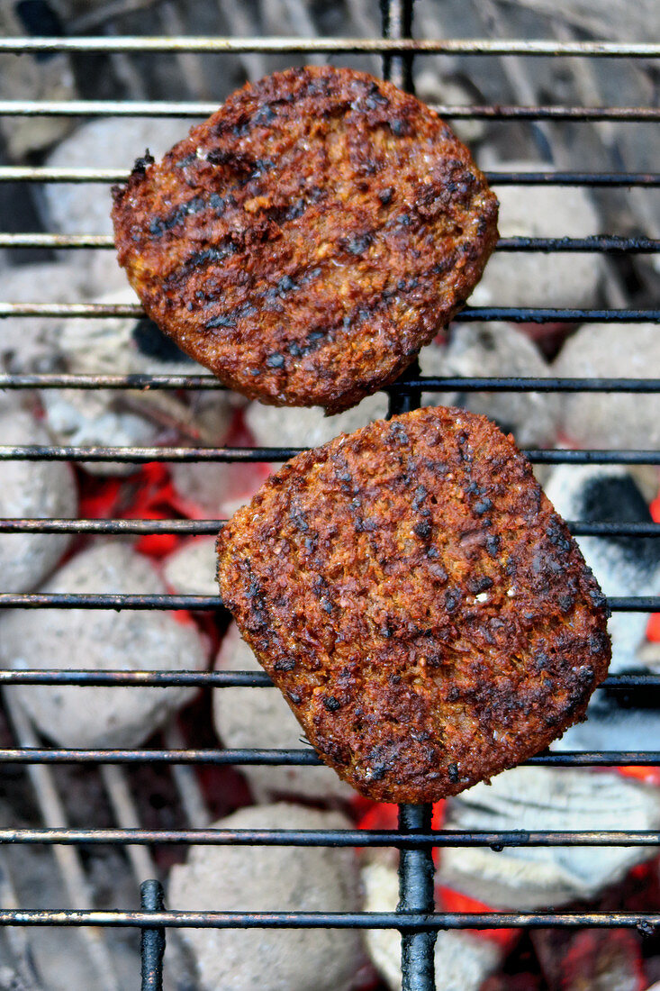 Vegane Burgerpatties auf Grillrost über Holzkohlegrill (Aufsicht)