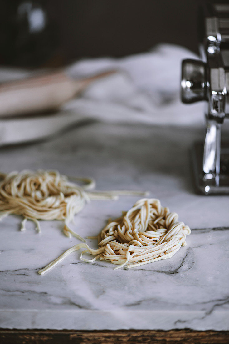 Selbstgemachte rohe Pasta auf Marmorarbeitsplatte neben Nudelmaschine