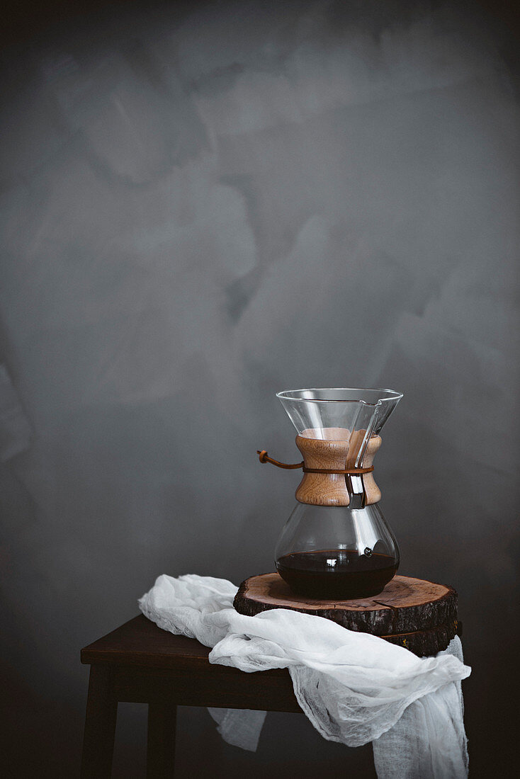 Chemex-Kaffeekaraffe auf Holzhocker vor grauem Hintergrund