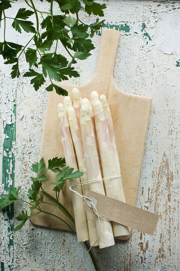 A bunch of white asparagus and parsley on a chopping board