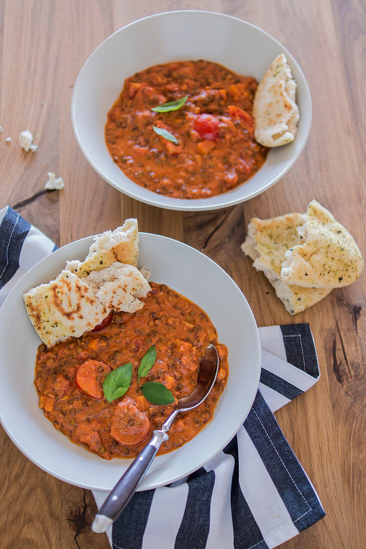 Linsencurry mit Kokos in zwei Tellern und Naan-Brot