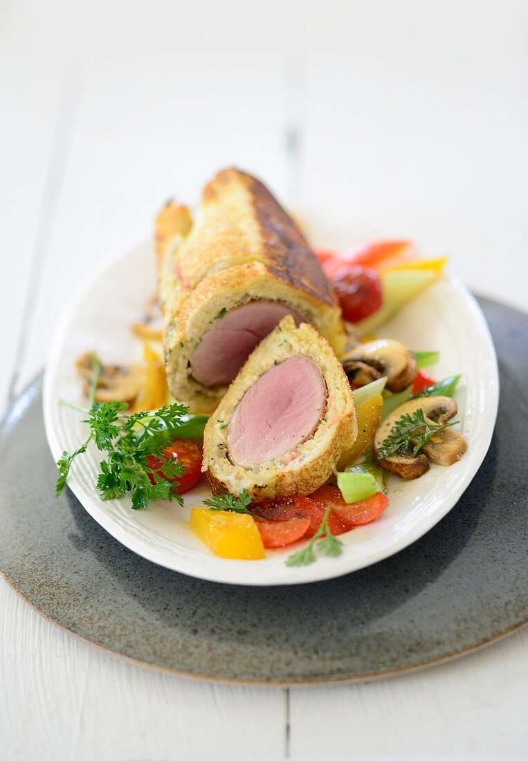 Aromatic fillet of pork wrapped in bread on a bed of peppers and mushrooms