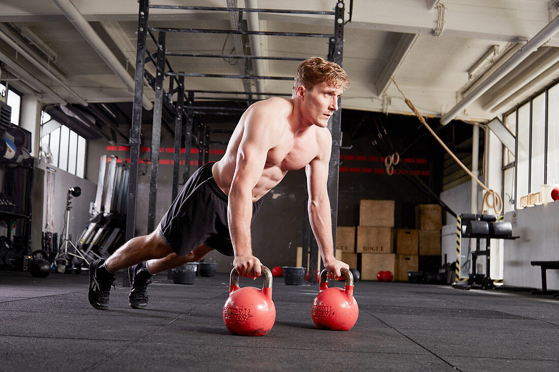 A young man performing jump throughs with kettlebells