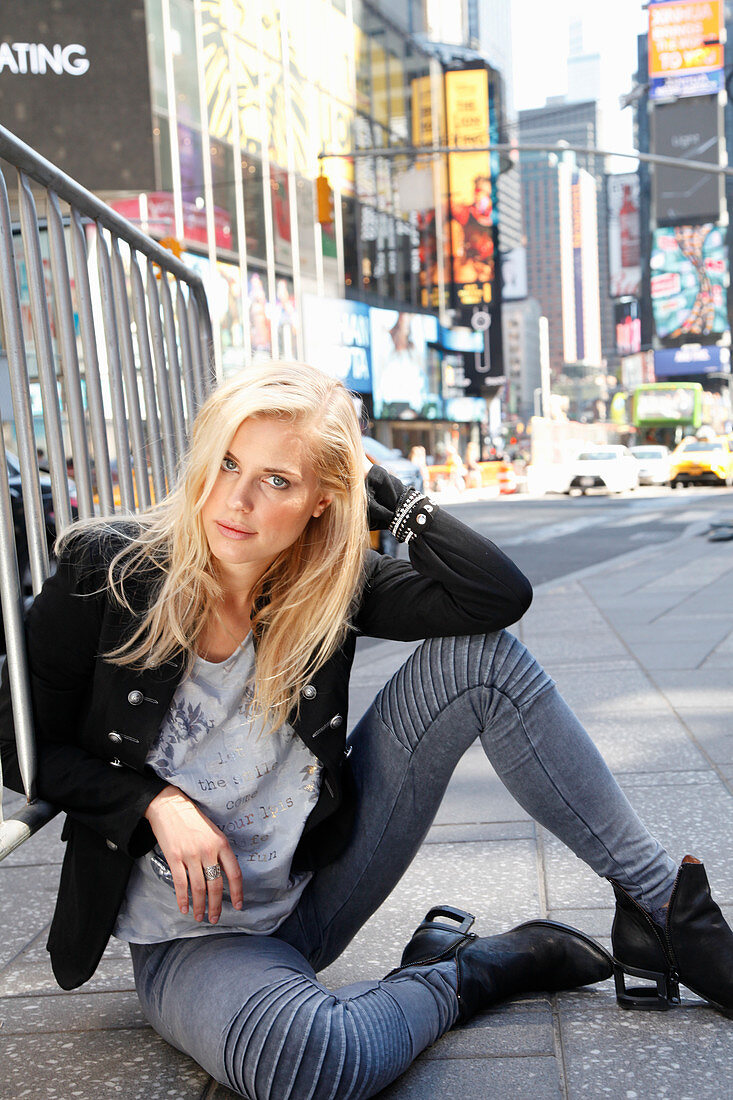 A blonde woman wearing a black blazer and grey jeans sitting on the floor