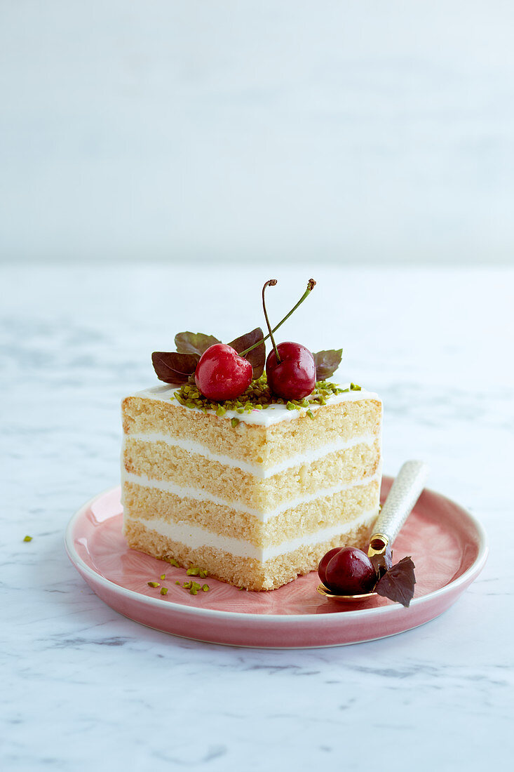 A slice of cake with a cream filling garnished with cherries and pistachios