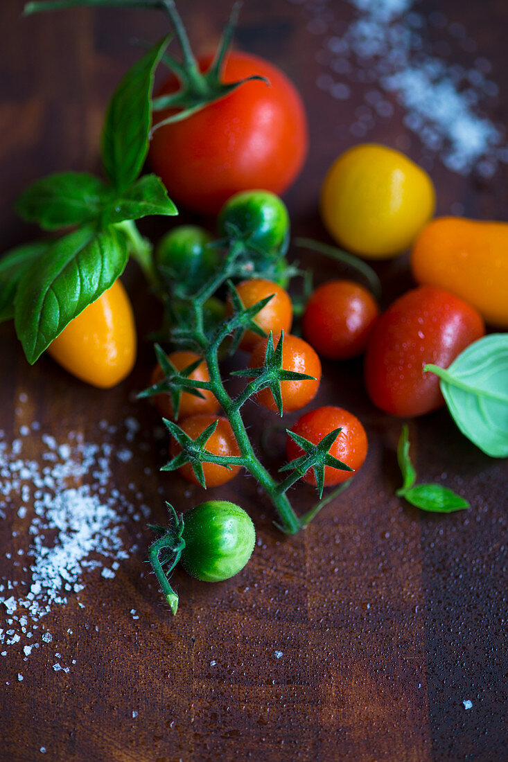 Various fresh mini tomatoes with basil and salt on a wooden surface