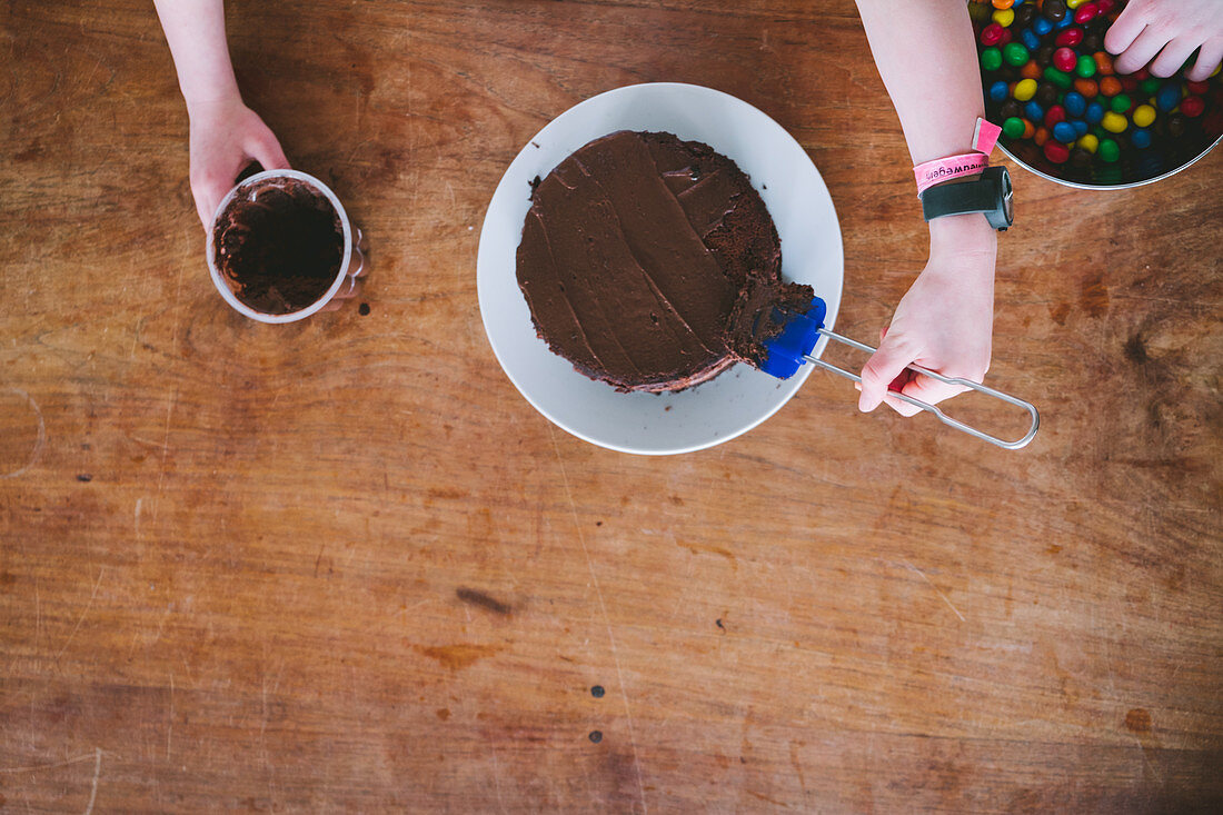 Two kids makeing chocolate cake for Mother's Day from above at a wooden table