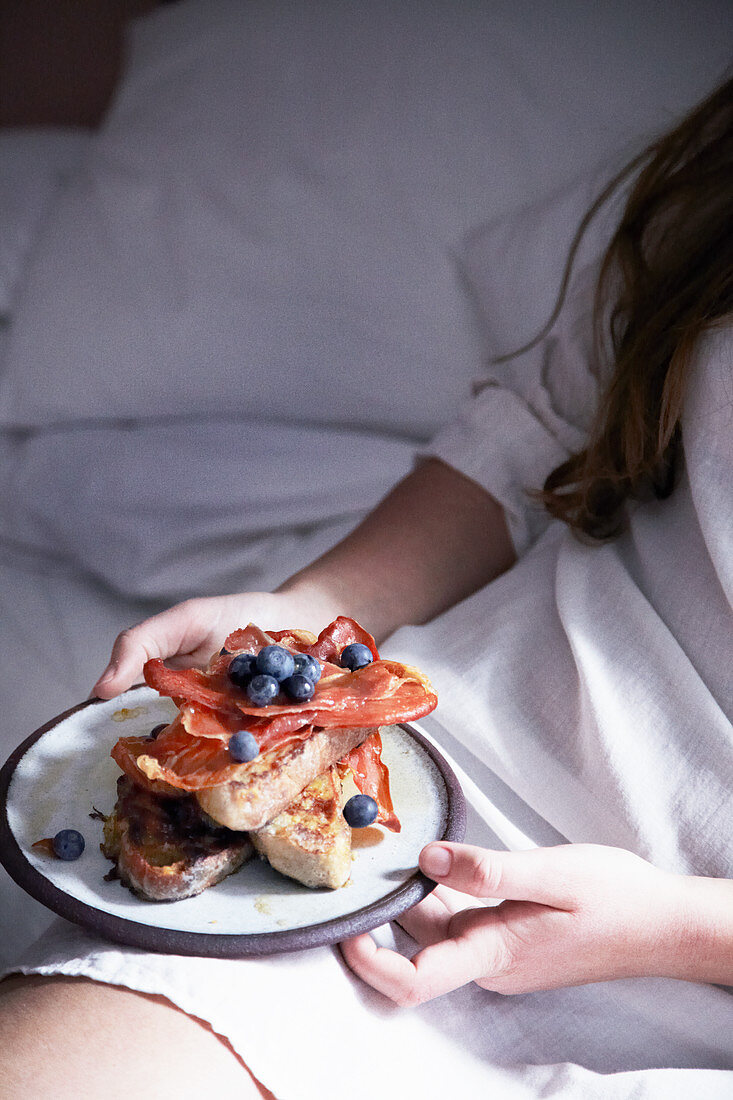 A woman having a breakfast of toast with bacon and blueberries in bed