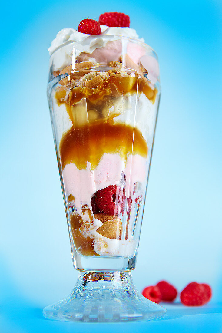 An ice cream sundae with raspberries, sauce and cream