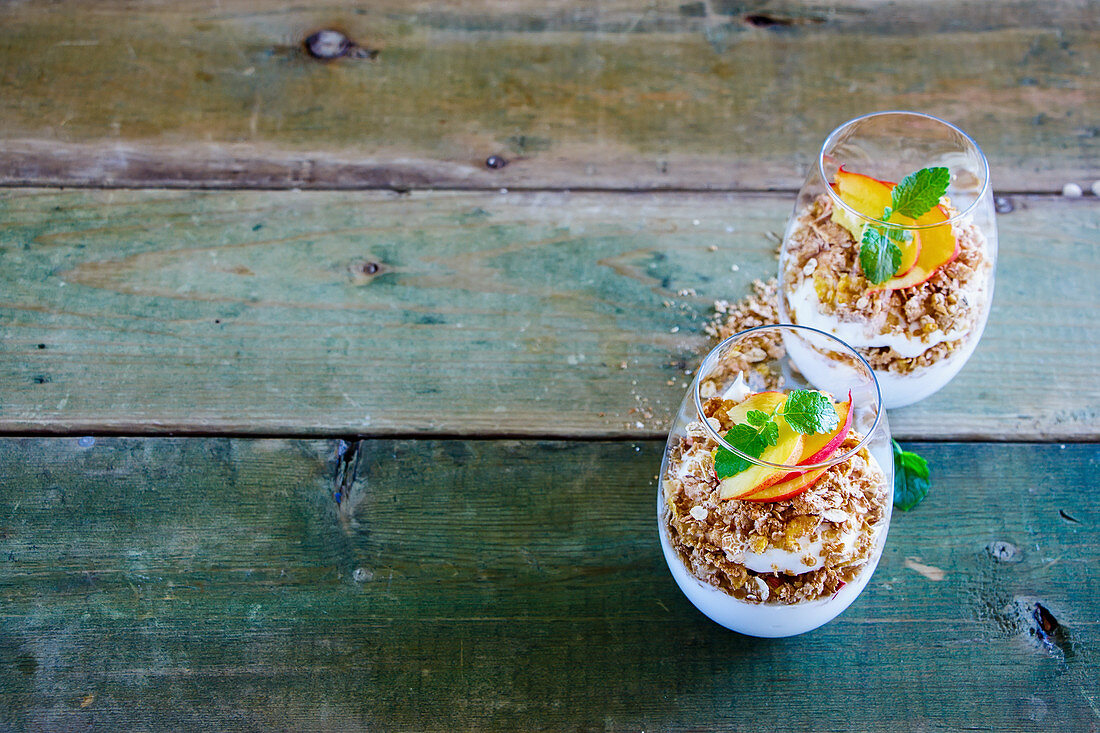 Detox Greek yogurt, granola, peach layered parfait in glasses with mint leaves