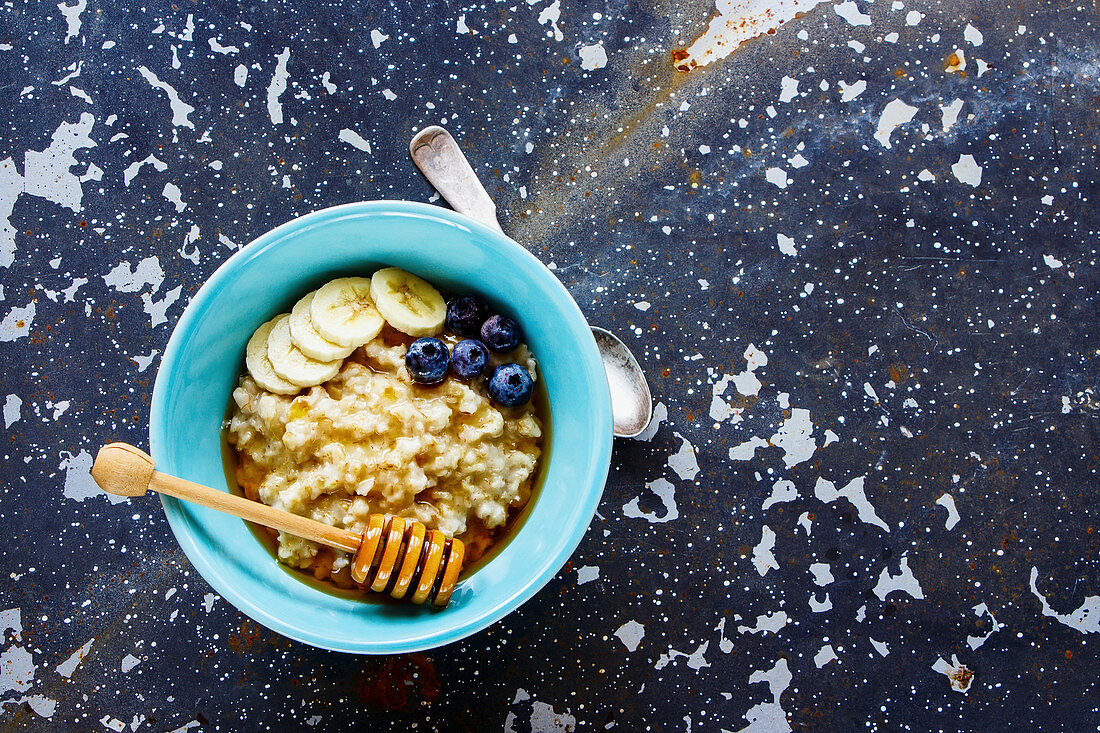 Bowl of classic oatmeal porridge with honey, banana and organic frozen blueberries