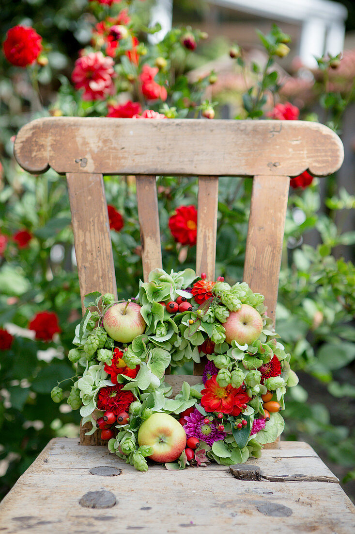 Late-summer wreath of hops, green hydrangeas, zinnias and apples on garden chair