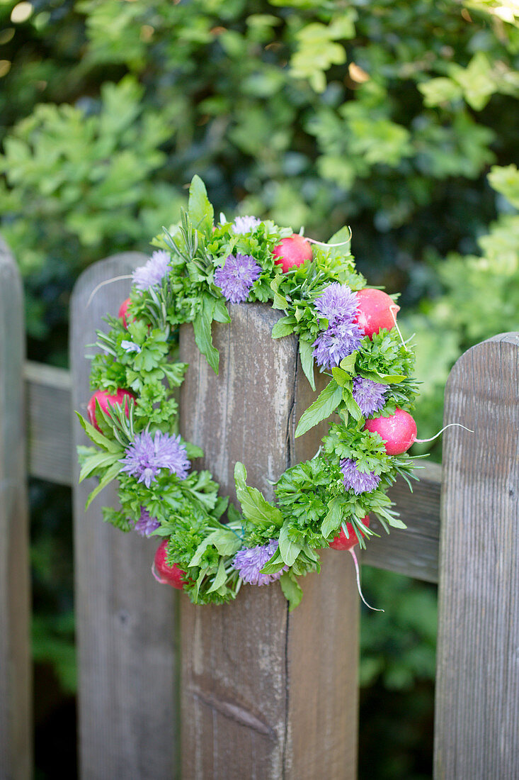 Handmade wreath of chive flowers, herbs and radishes on wooden fence