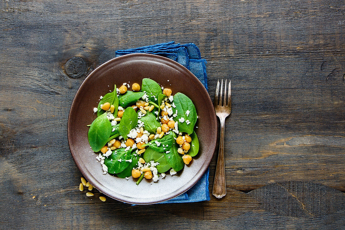 Organic energy boosting salad with spinach leaves, chickpeas, pine nuts and feta cheese on wood background