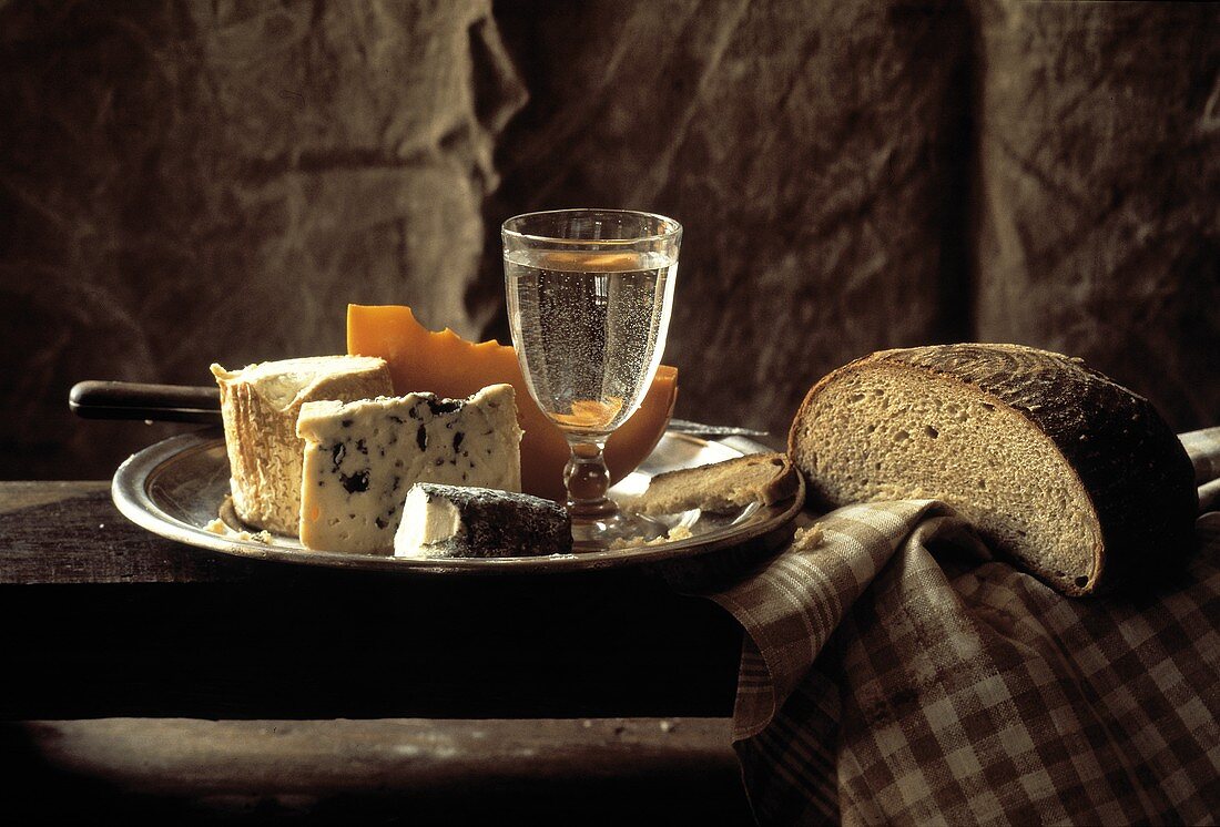 Teller mit Käse, Kürbis, Wasserglas & Brot auf Holztisch