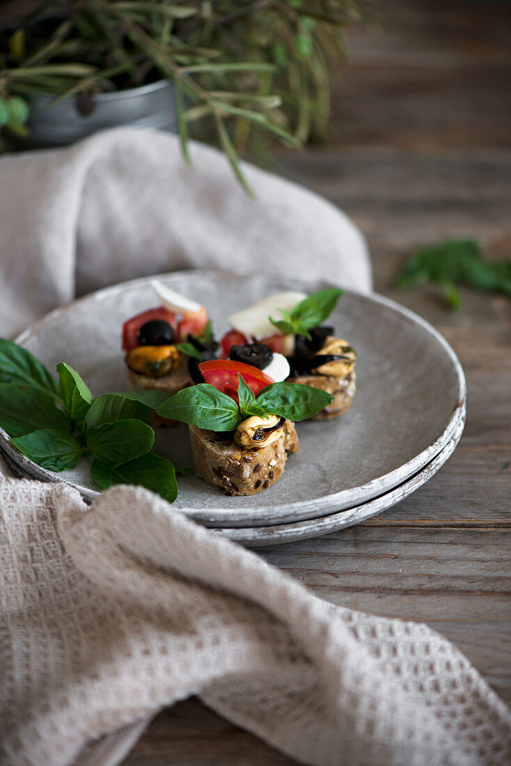 Crostini with mozzarella, olives, mussels, tomatoes, and basil leaves