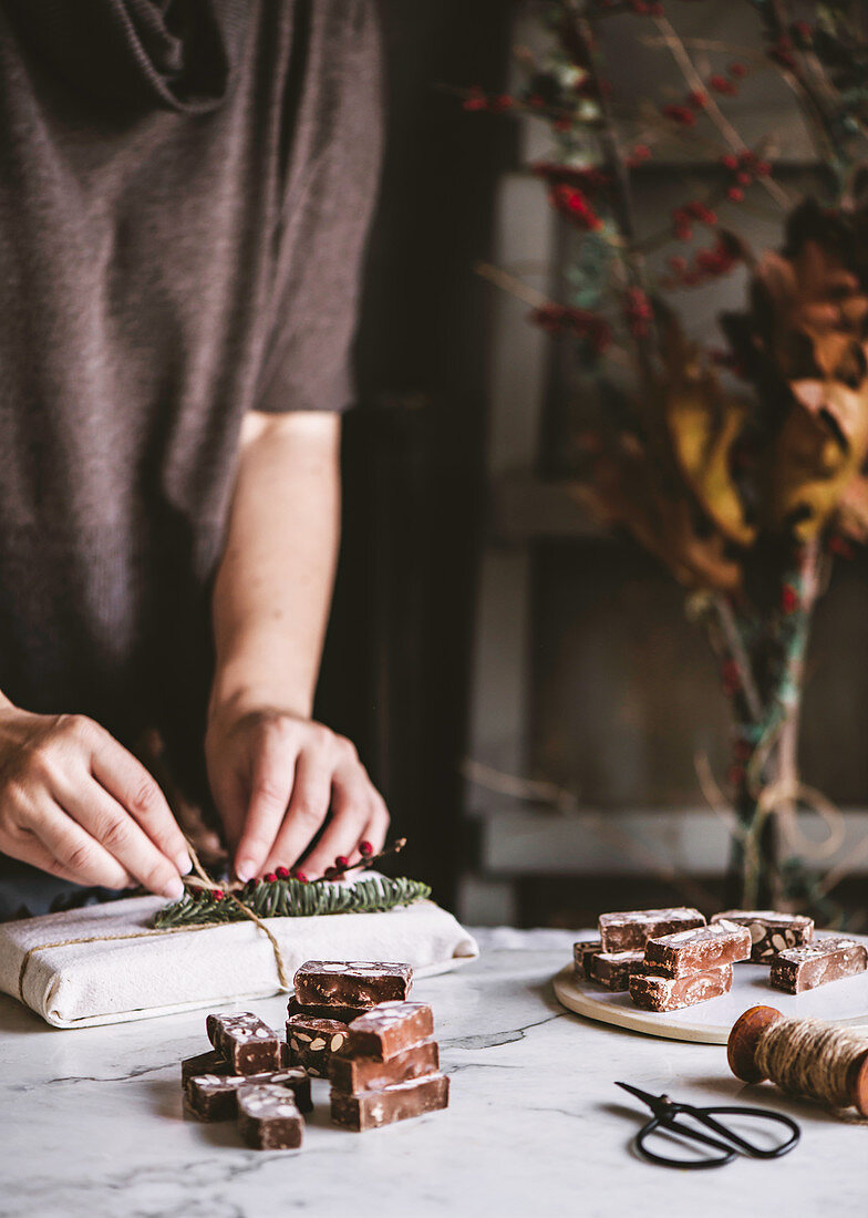 Person wrapping and decorating present with chocolate nougat candy