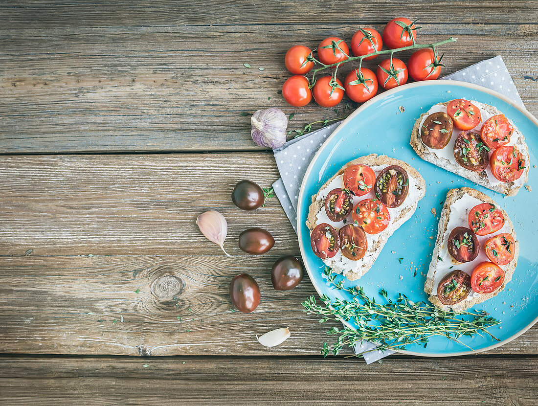 Rustic breakfast set of sandwiches with soft cream-cheese, cherry-tomatoes roasted with garlic and thyme