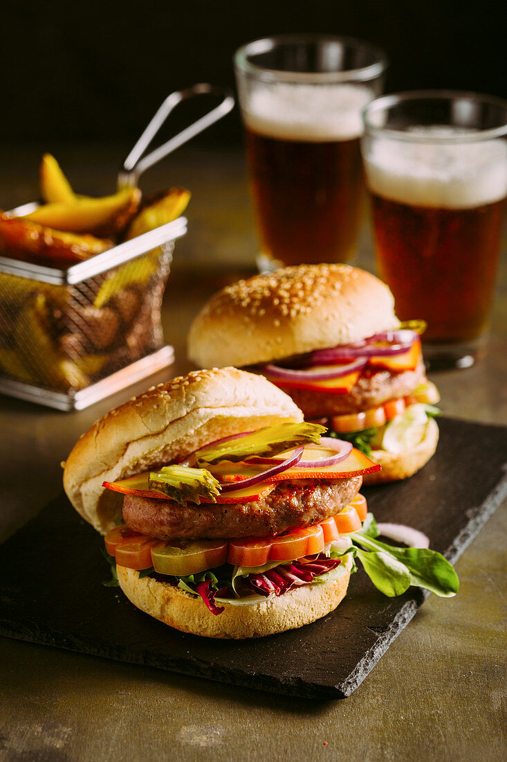 Gourmet-Burger mit Hähnchenfleisch, Käse, Tomaten, Salat und Zwiebeln, dazu Pommes und Bier