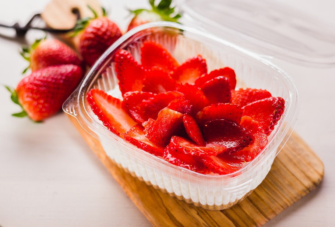 Geschnittene Erdbeeren mit Sahne im Plastikbehälter