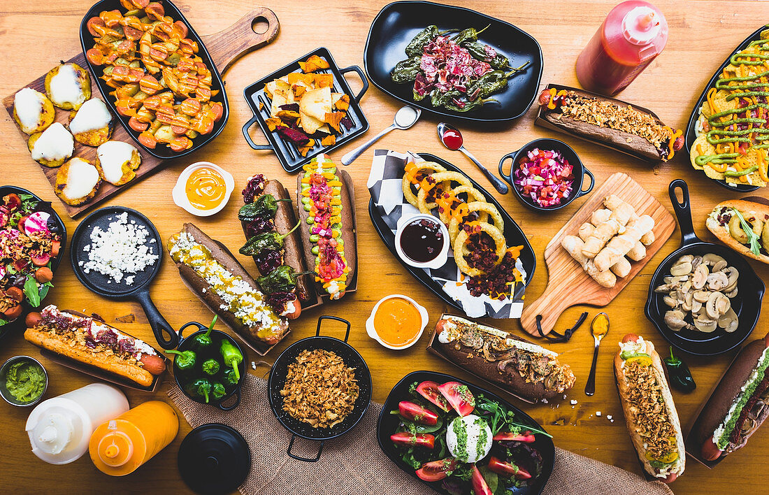 Viele verschiedene Snacks und Hot Dogs mit Saucen und Gewürzen auf Holztisch