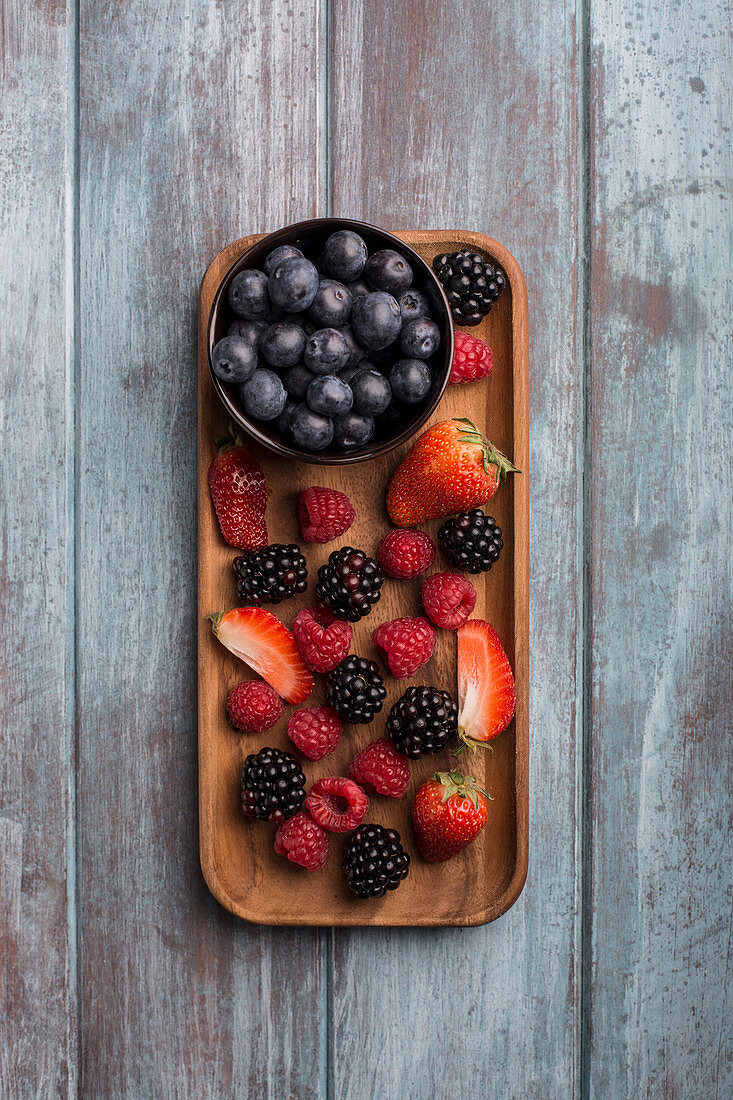 Frische Beeren im Schälchen und auf Servierplatte aus Holz (Aufsicht)