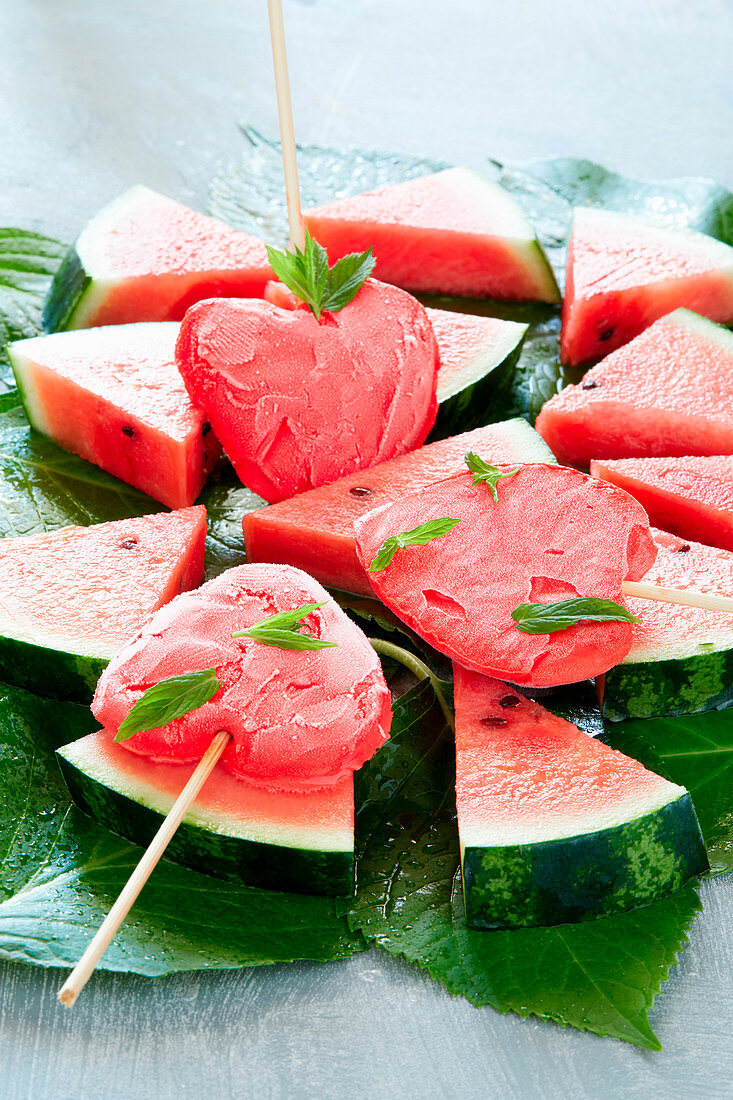 Herzförmiges Wassermeloneneis am Stiel auf Wassermelonenscheiben