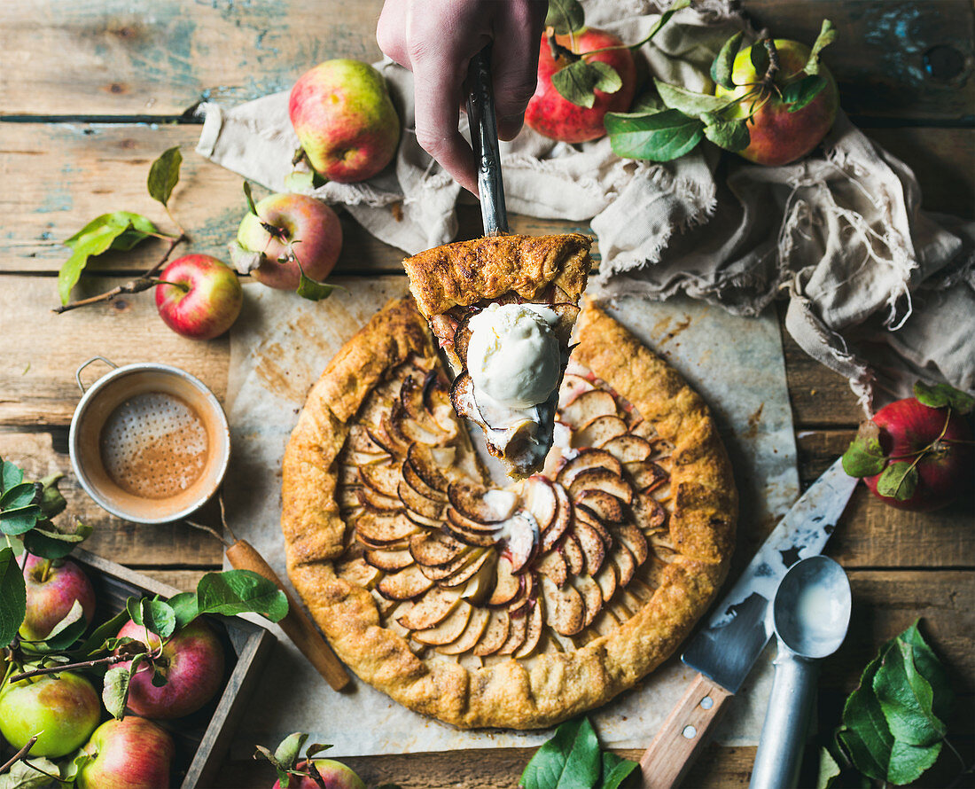 Man's hand holding piece of apple crostata with cinnamon and ice-cream scoop