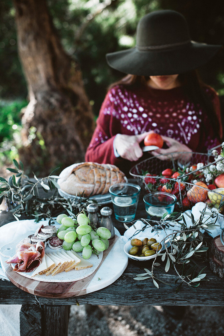 Woman in black hat sitting at table and cutting fruits and vegetables for lunch