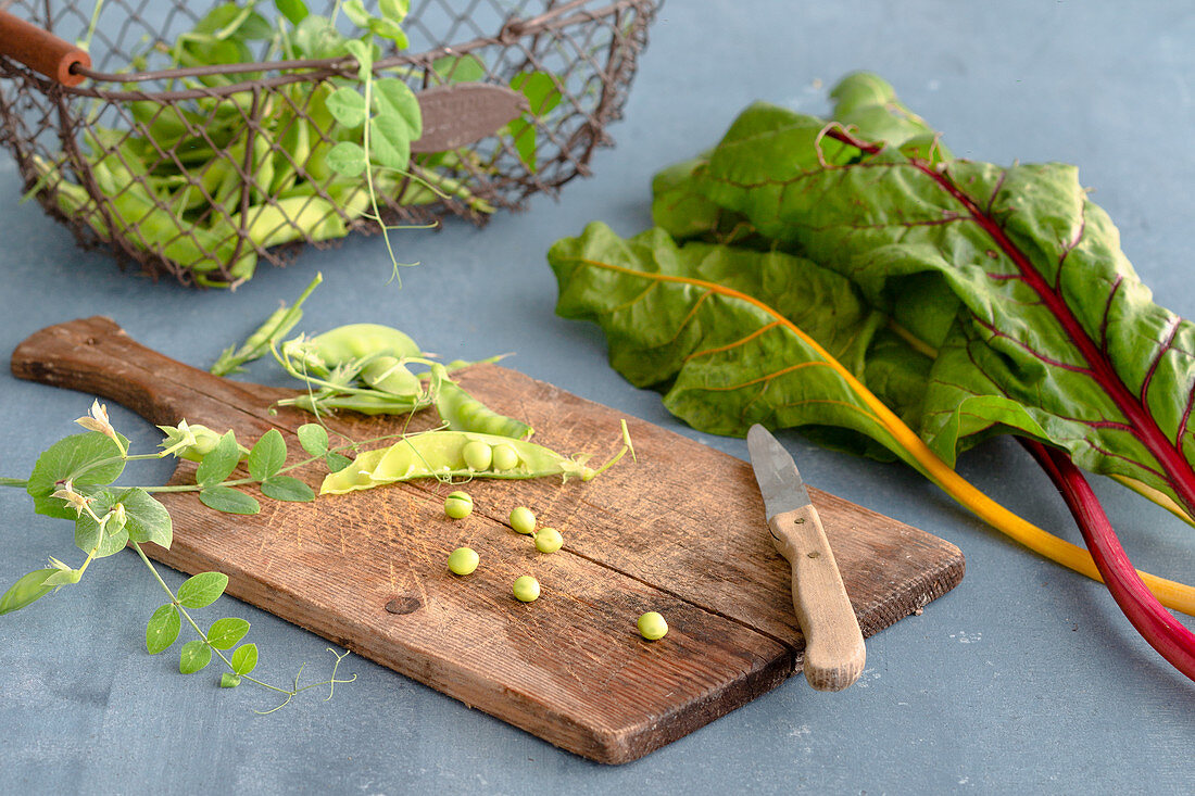 Pea pods on a wooden board next to colourful chard stems