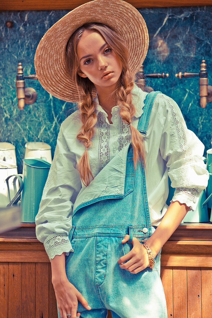 A young woman wearing a straw hat, a light blue blouse with lace trim and dungarees