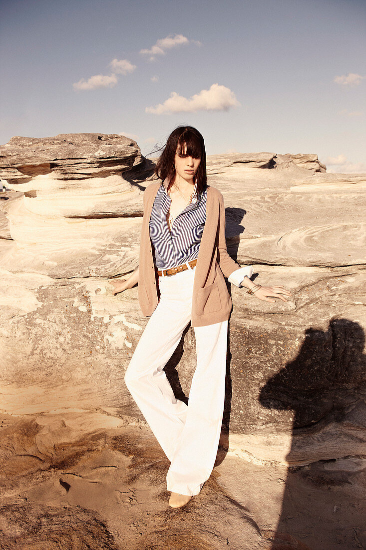 A brunette woman wearing a striped blouse, a cardigan and white trousers