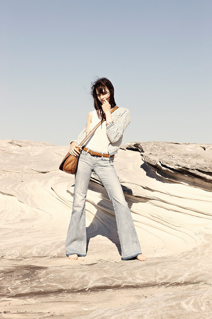 A brunette woman with a shoulder bag wearing a white top, a jacket and jeans