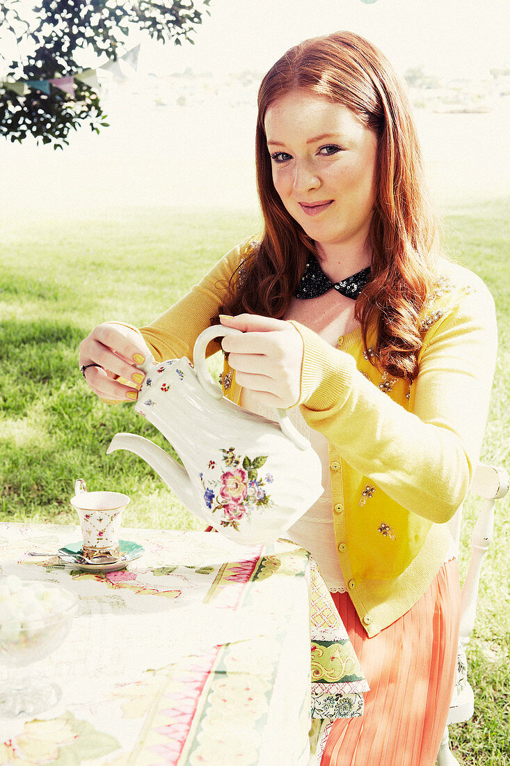 A young woman with a teapot at a garden table