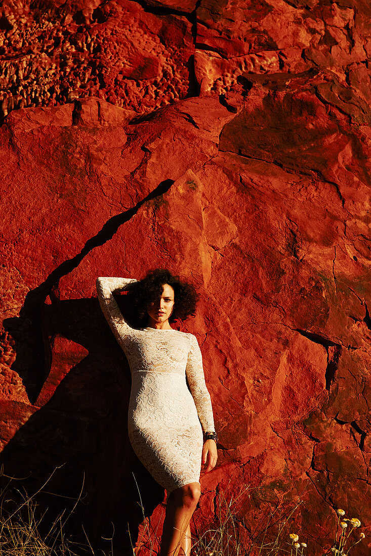 A young woman wearing a white lace dress standing against red rocks