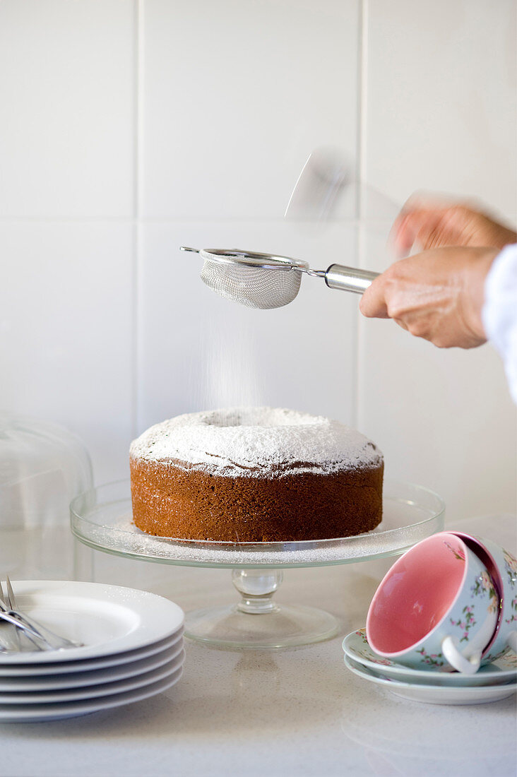 A sponge cake being dusted with icing sugar