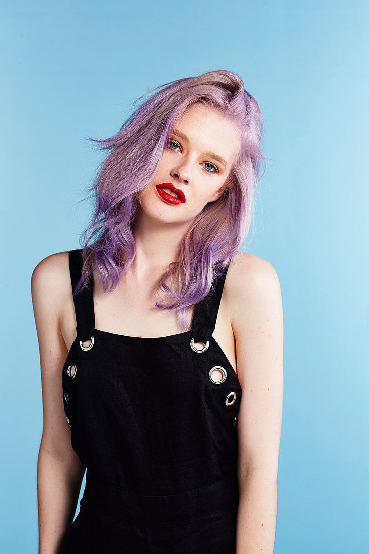 A young woman with pink hair wearing black dungarees