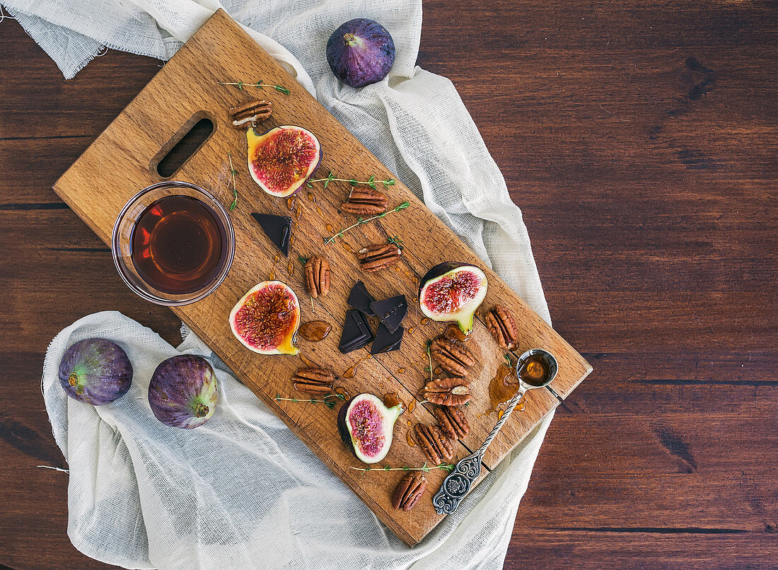 Fresh figs, bitter chocolate and pekan nuts with honey on a wooden board and white tissue